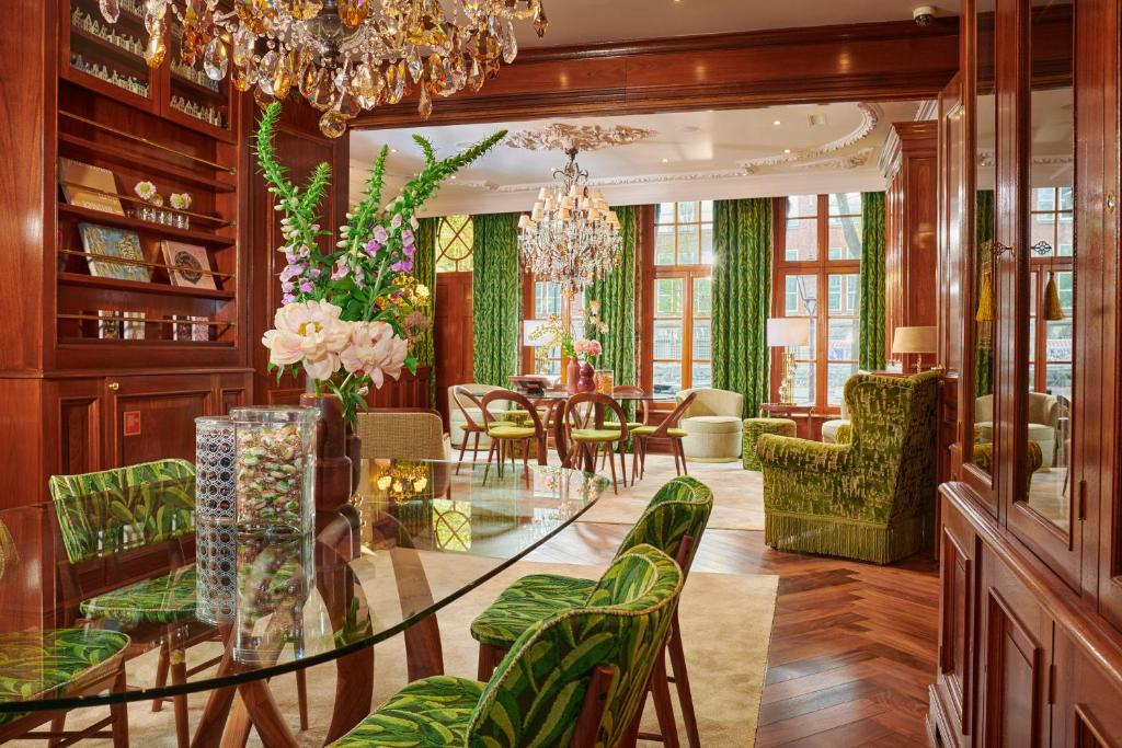 Foto do Hotel Estheréa. Sala de jantar e sala de estar com painéis de madeira, cadeiras com estampa verde, lustres e janelas grandes com cortinas verdes.