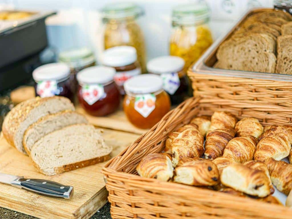 Foto do ibis Styles Amsterdam City. Pão fatiado, croissants em uma cesta e potes de geleia e conservas em uma mesa de bufê de café da manhã.