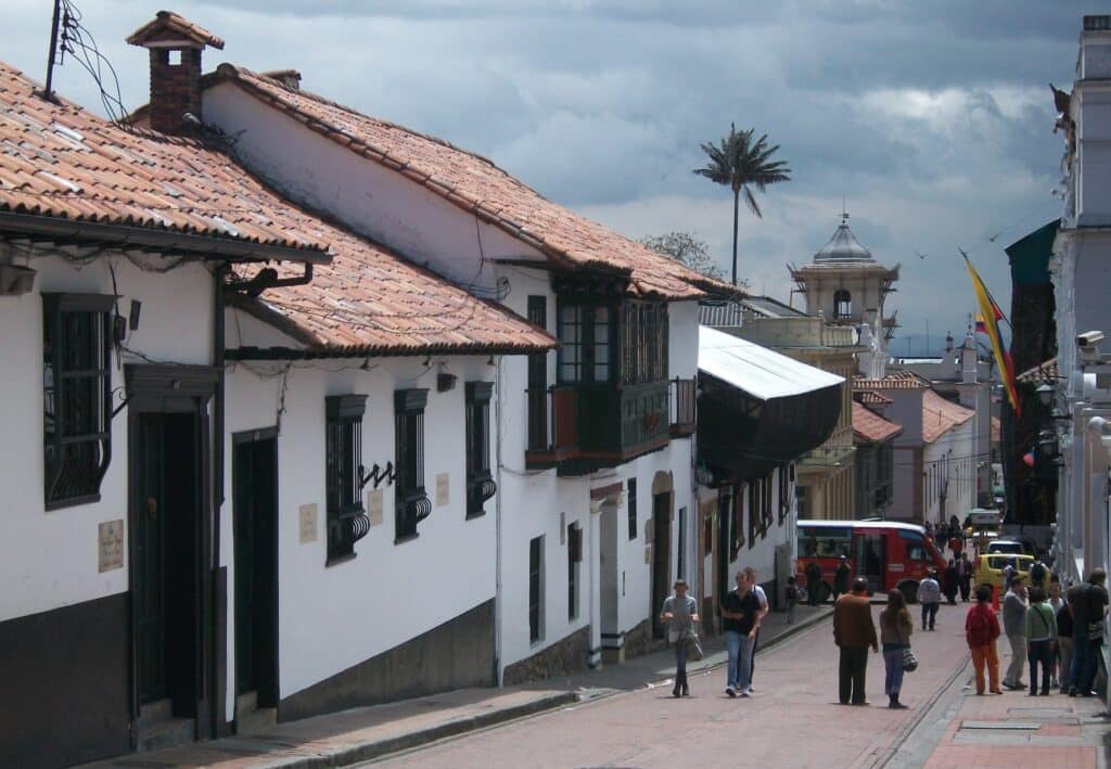 As pessoas caminham por Carrera 4, com por edifícios brancos em estilo colonial sob um céu nublado.