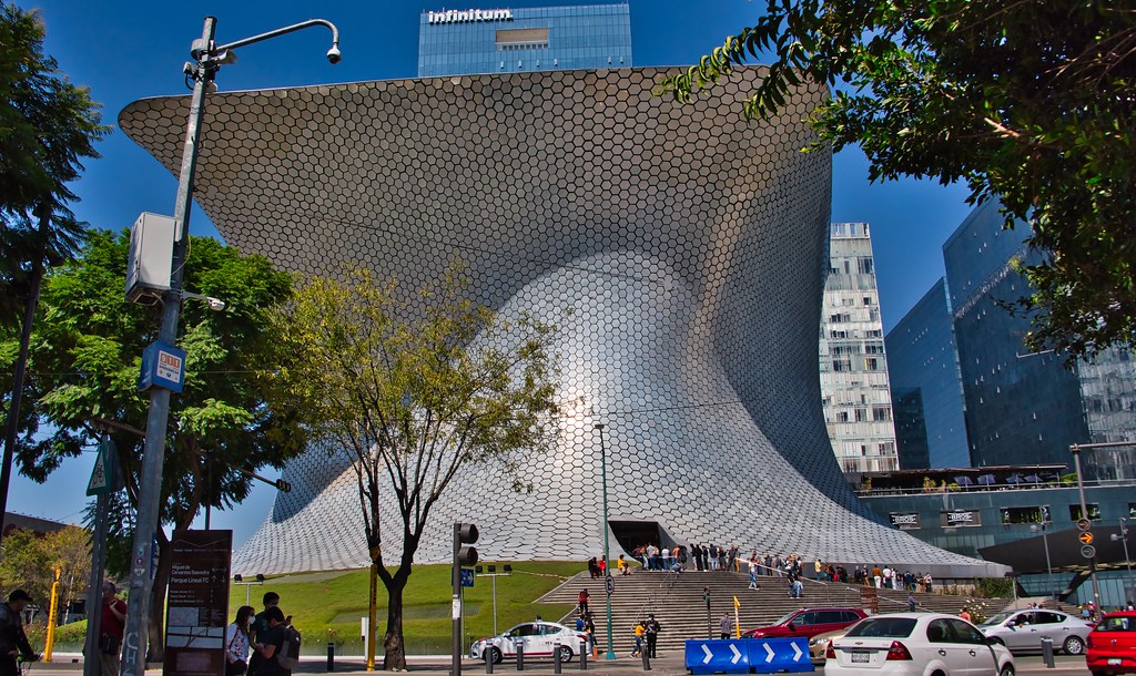 Museu Soumaya com um exterior de padrão hexagonal, pessoas em degraus, árvores e carros na frente, no bairro Polanco. Imagem para ilustrar post sobre onde ficar na Cidade do México.