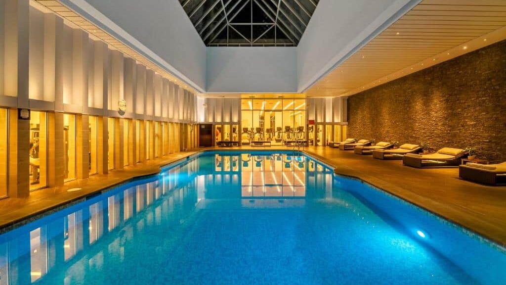 Piscina interna do Hyatt Regency Mexico City com espreguiçadeiras em um dos lados, parede de pedra e teto de vidro acima, iluminado com luzes quentes. Imagem para ilustrar post sobre onde ficar na Cidade do México.