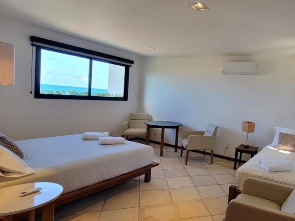 Quarto do Arandu Sagi Inn, uma das pousadas em Baía Formosa, espaçoso com uma cama, cadeiras, uma mesa pequena, janela grande com vista para o mar e piso de azulejos.
