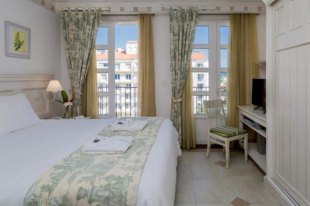 Quarto do IL Campanario Villaggio Resort com uma cama de casal, janelas com cortinas verdes, uma TV na parede e uma cadeira ao lado de uma pequena escrivaninha.