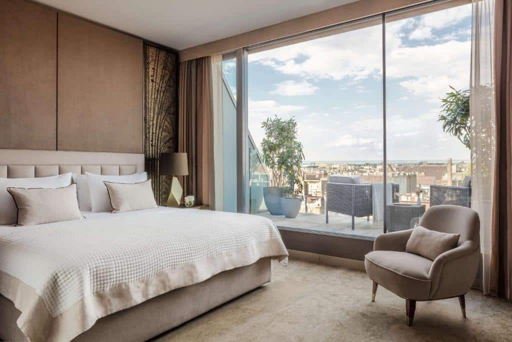 Um quarto do Anantara New York Palace com uma cama grande, poltrona e janela do chão ao teto com vista para um terraço e para o horizonte da cidade.