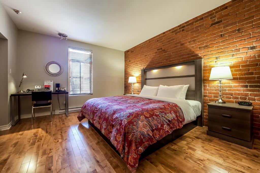 Um quarto do Auberge de La Fontaine com uma parede de tijolos, cama king-size, duas mesinhas de cabeceira, luminárias, uma escrivaninha e piso de madeira.