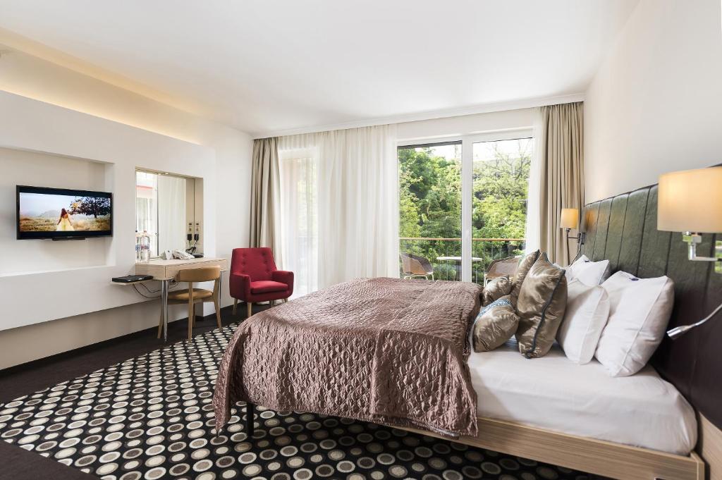 Quarto do Bo33 Hotel Family & Suites com uma cama de casal, TV, escrivaninha, cadeira vermelha, janela grande e carpete estampado.