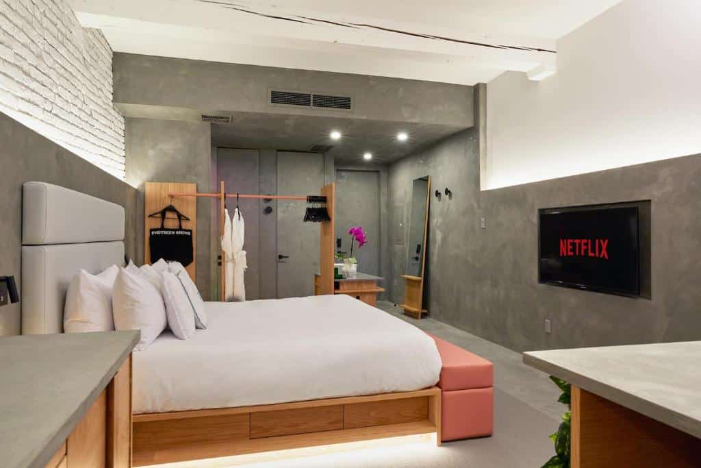 Quarto do David Hotel com uma cama, TV na parede exibindo "Netflix", roupões em cabides e decoração minimalista.