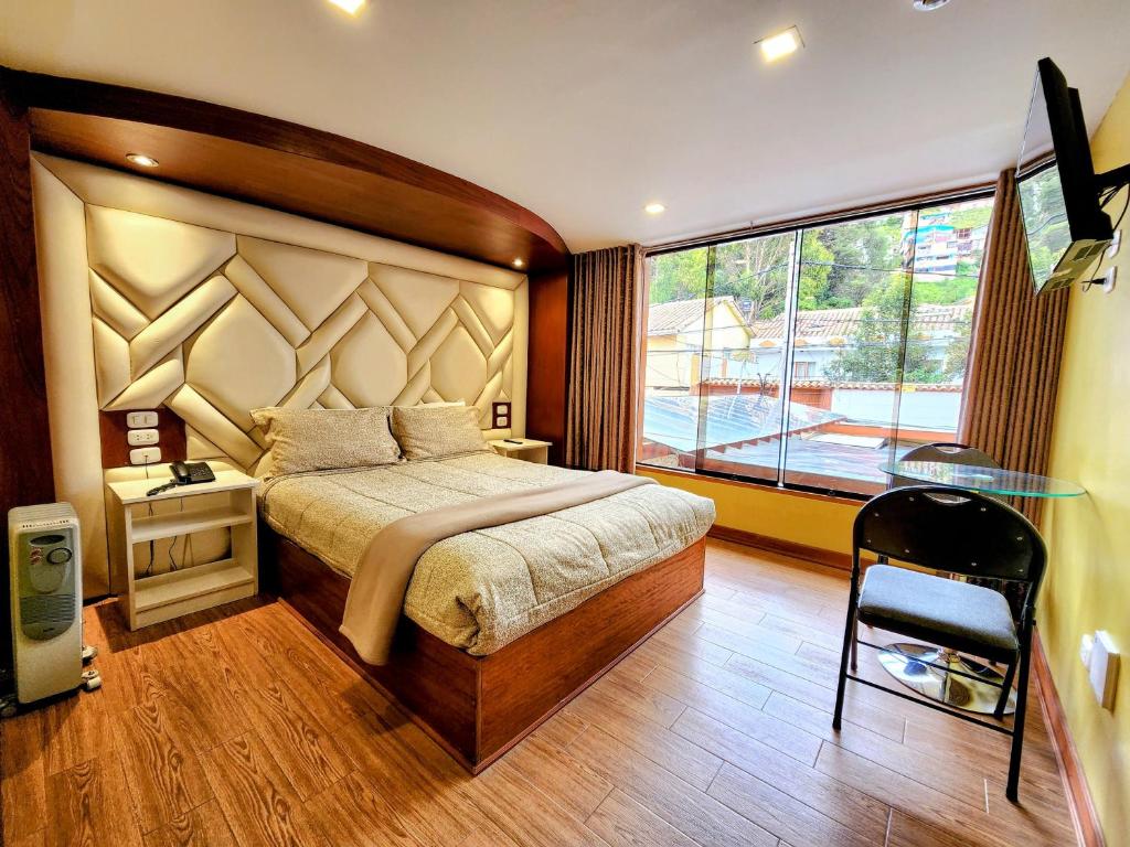 Uma cama bem arrumada em um quarto do hotel El Mariscal Cusco bem iluminado com piso de madeira, janelas grandes e uma pequena escrivaninha com uma cadeira.