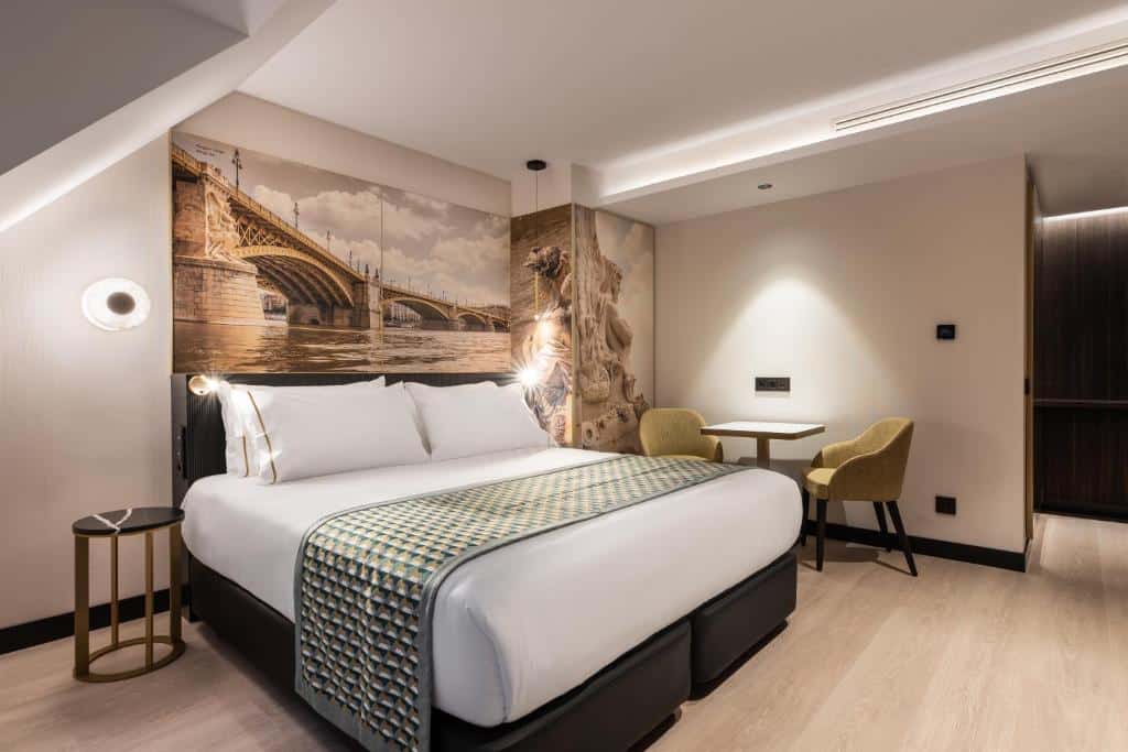 Quarto do Eurostars Ambassador com uma cama grande, mesa pequena com duas cadeiras, arte na parede e decoração em cores neutras.