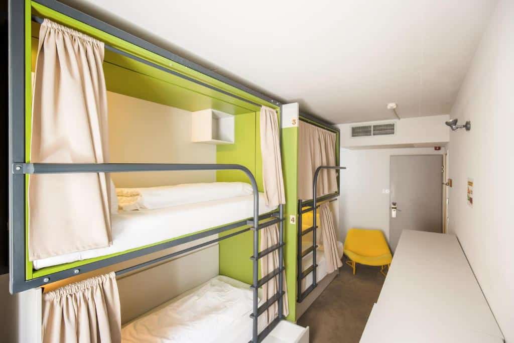 Um quarto do Maverick Central Market com dois beliches com cortinas, uma cadeira amarela, uma escrivaninha branca e uma porta na extremidade oposta.