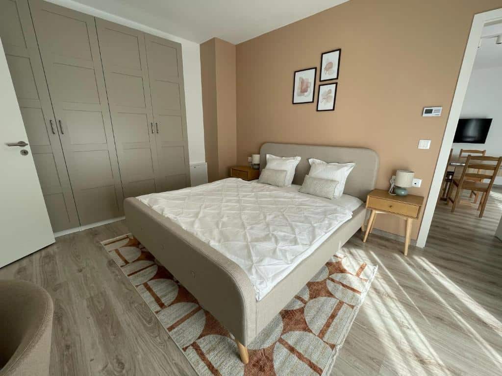 Uma cama de casal do MT Suites ApartHotel bem arrumada em um quarto moderno com paredes bege, duas mesinhas de cabeceira e um grande guarda-roupa.