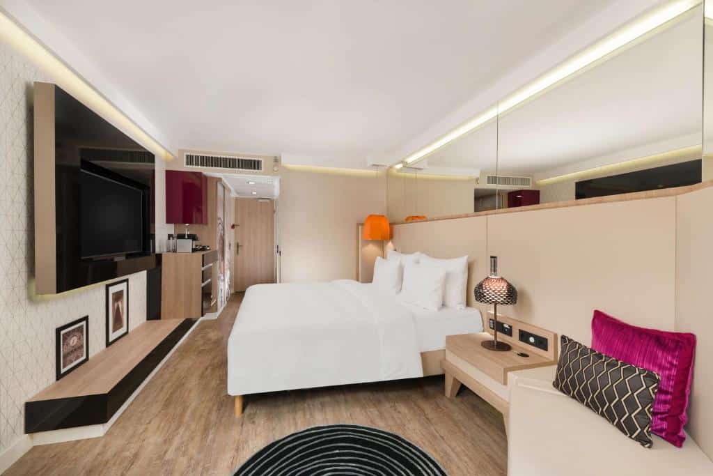 Quarto do Radisson Blu Béke Hotel com uma cama grande, TV na parede, poltrona, mesas laterais e decoração contemporânea.