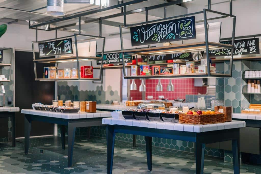 Foto do Stayokay Hostel. Um buffet de café da manhã self-service com cereais, doces, frutas e bebidas em balcões modernos em uma área de jantar bem iluminada.