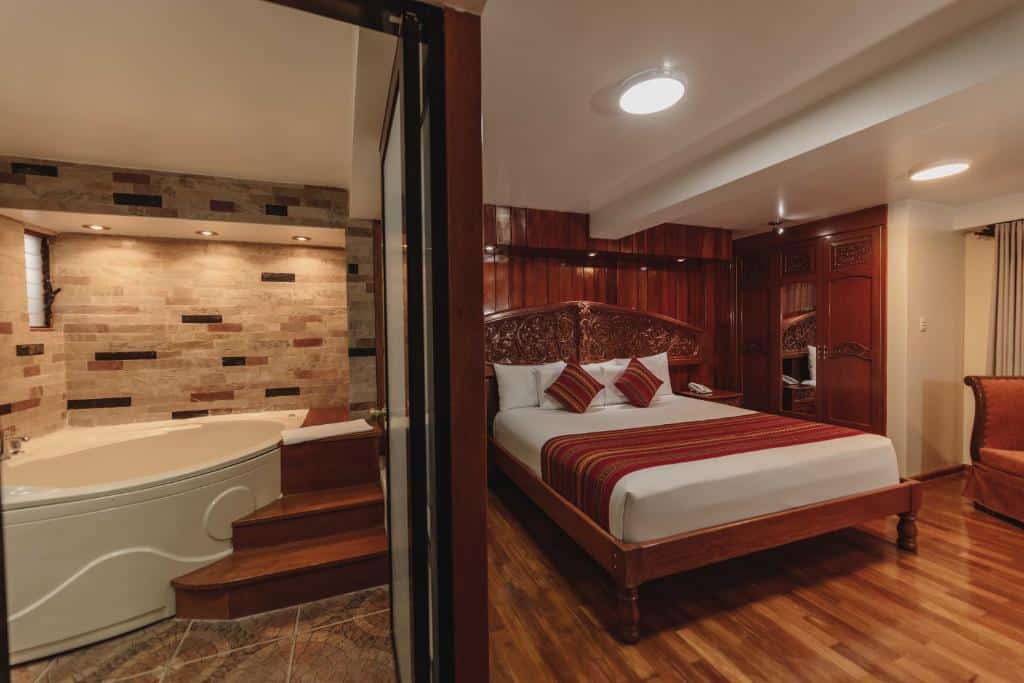 Quarto do Quechua Hotel Cusco com uma cama grande, móveis de madeira e banheira de hidromassagem no quarto com detalhes em azulejo.