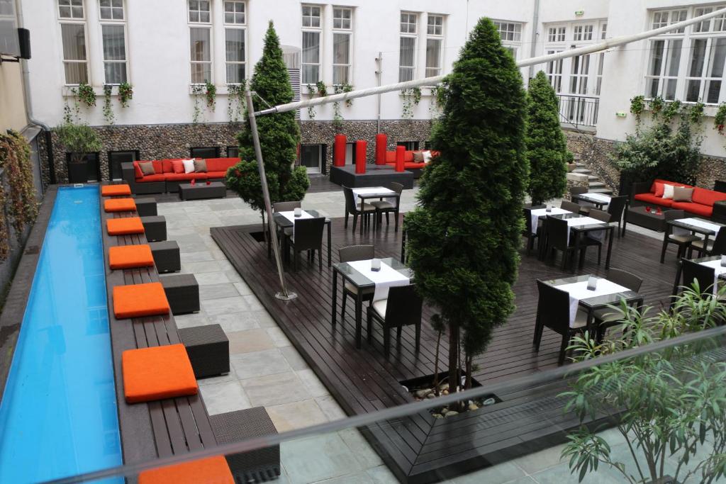 Pátio moderno com árvores altas, mesas e cadeiras pretas, bancos com almofadas vermelhas e uma piscina retangular estreita, no Levante Parliament.