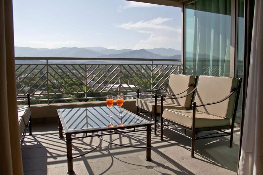 Uma varanda com grades de metal no Amérian Executive Hotel em Mnedoza, duas cadeiras, uma mesa de vidro e dois copos de laranja tem vista para as montanhas distantes.