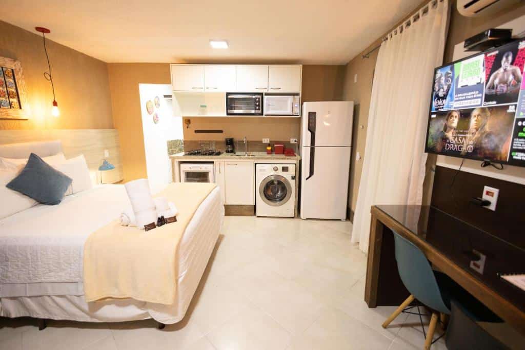Apartamento estúdio da Pousada Reserva, com cama, utensílios de cozinha, geladeira, máquina de lavar, TV e mesa com cadeira.