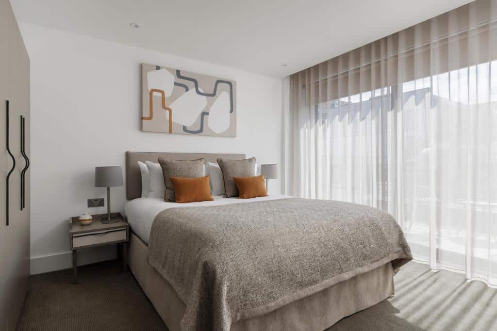 Quarto moderno no Forth House com uma cama de casal, arte abstrata acima da cabeceira, duas mesas de cabeceira e cortinas transparentes do chão ao teto.