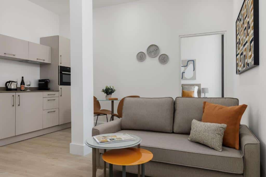 Sala de estar moderna no Forth House com sofá bege, pequenas mesas redondas, uma área de cozinha, mesa de jantar e arte na parede em um esquema de cores neutras.