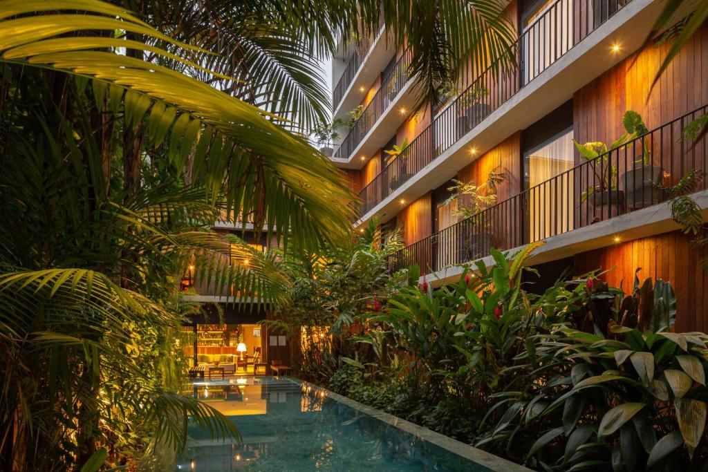 Um moderno edifício do Hotel Villa Amazônia com varandas tem vista para uma estreita piscina externa cercada por exuberantes plantas tropicais ao anoitecer. Representa hotéis em Manaus.