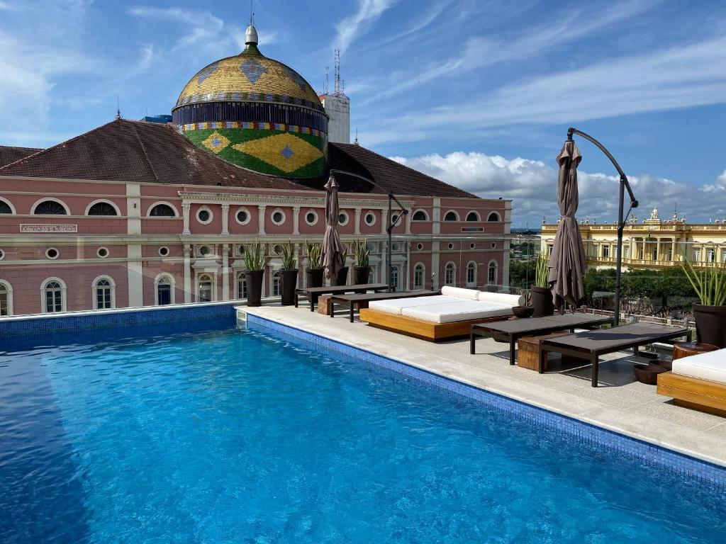 Piscina na cobertura com espreguiçadeiras com vista para um edifício histórico abobadado sob um céu azul com nuvens, do Juma Ópera Boutique Hotel & Spa. Representa hotéis em Manaus.