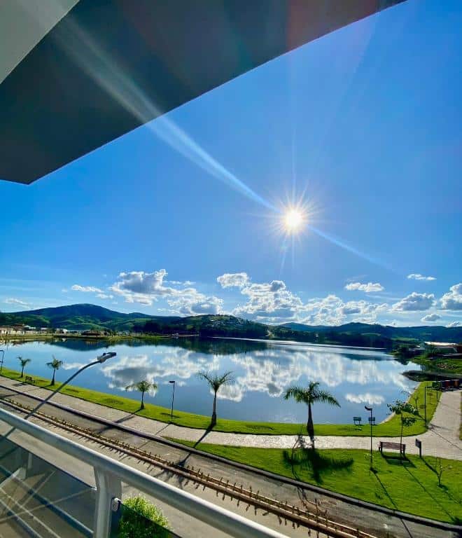 Um dia ensolarado com céu azul claro, um lago calmo, palmeiras e colinas distantes vistas de uma varanda, do Lara's Hotel. Representa hotéis em Capitólio.