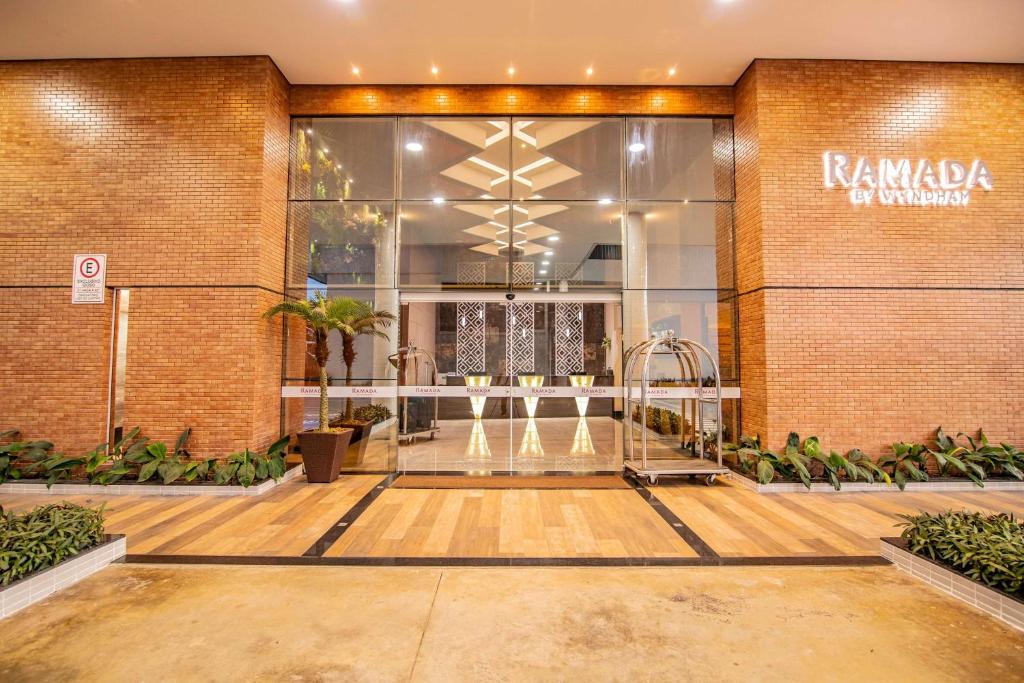Entrada de vidro de um hotel moderno com paredes de tijolos, vasos de plantas e a placa "Ramada by Wyndham" à direita. Representa hotéis em Manaus.