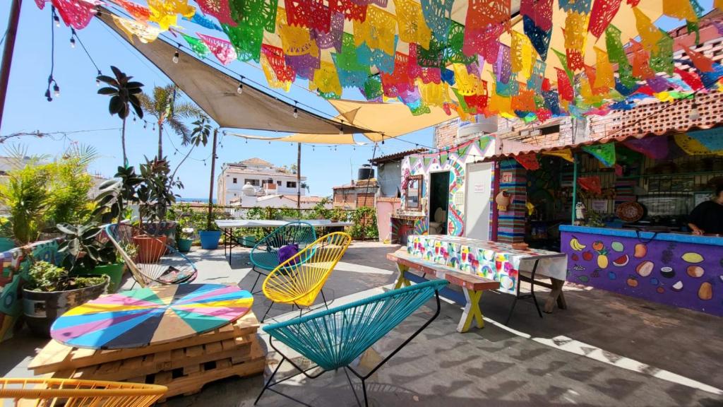 Pátio colorido ao ar livre do Hostel Vallarta com faixas festivas de papel picado, cadeiras vibrantes, mesas e plantas sob guarda-sóis.