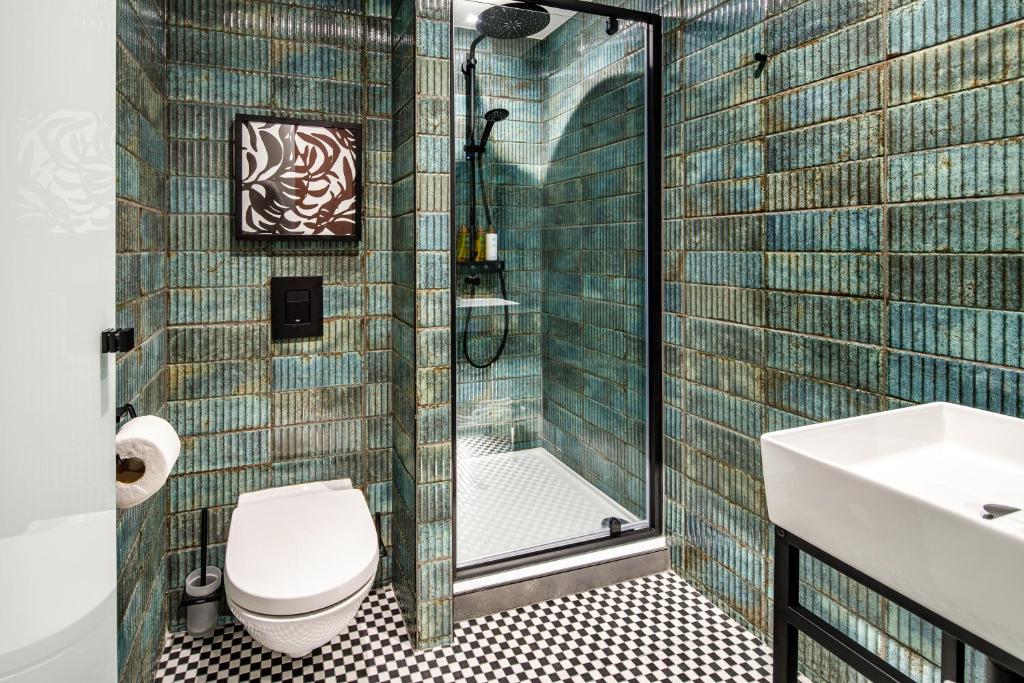 Banheiro moderno no ibis Styles Edinburgh com paredes de azulejos verdes, chuveiro, vaso sanitário de parede e pia branca com acessórios pretos. Ilustra o post de onde ficar em Edimburgo.