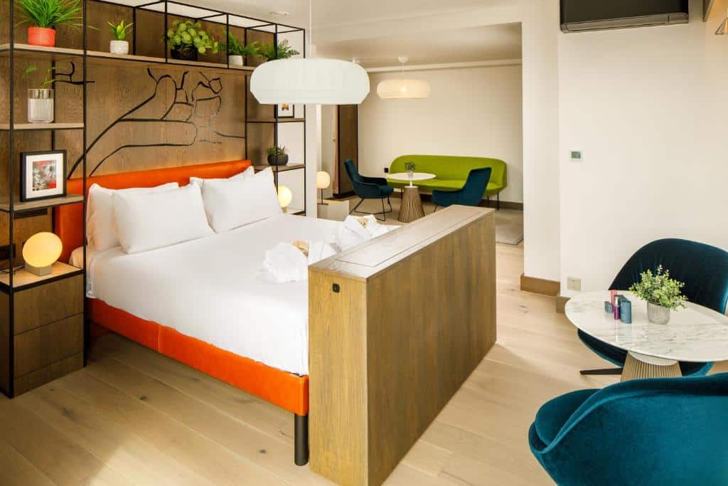 Quarto de hotel moderno no ibis Styles Edinburgh com uma cama de casal, divisória de madeira, área de estar e decoração contemporânea com detalhes em verde e azul. Ilustra o post de onde ficar em Edimburgo.