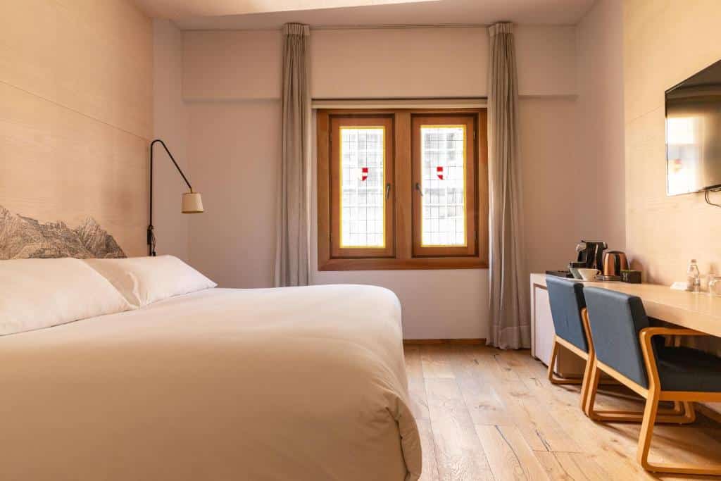 Um quarto do Hotel Magnolia Santiago com uma cama grande, uma janela com cortinas, uma escrivaninha, duas cadeiras, uma TV e uma chaleira em um piso de madeira.