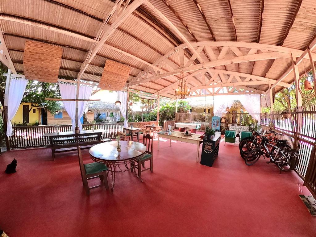 Pátio coberto com piso vermelho, mesas, cadeiras, bicicletas e cortinas brancas; um gato preto está sentado perto de uma mesa, da Pousada Ocazum. Representa hotéis em Alter do Chão.