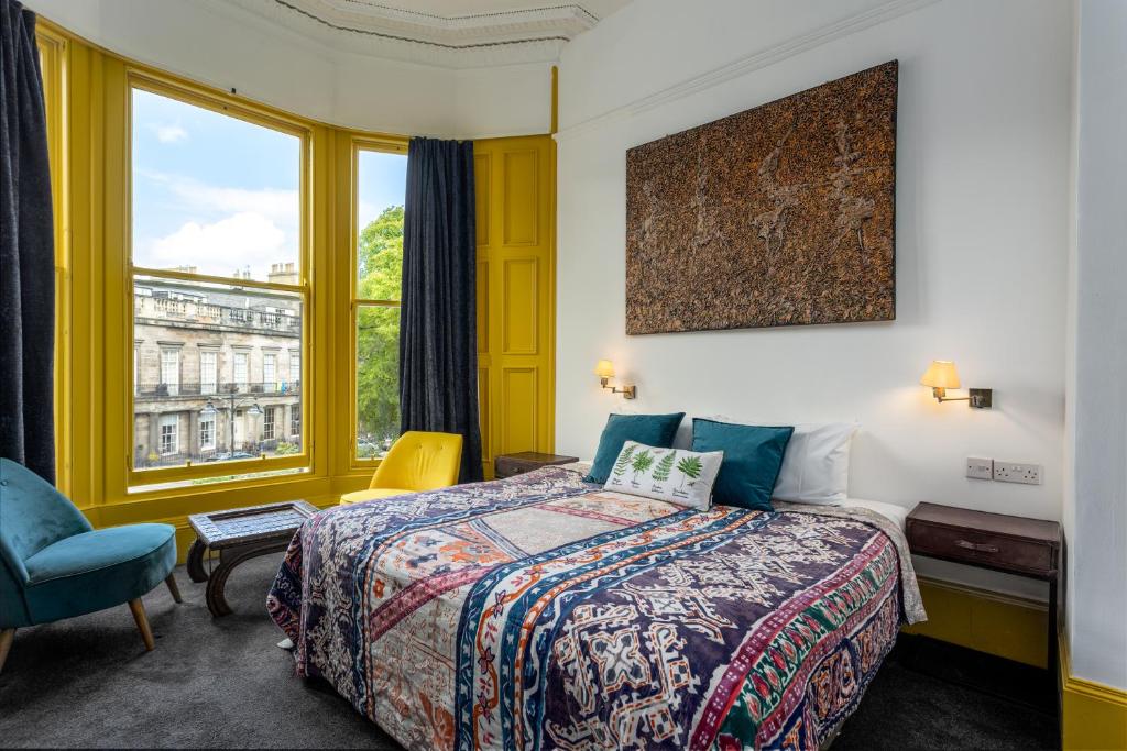Um quarto com colcha estampada no New Town Guest House, janela de sacada com moldura amarela, cadeira azul e arte na parede acima da cama.