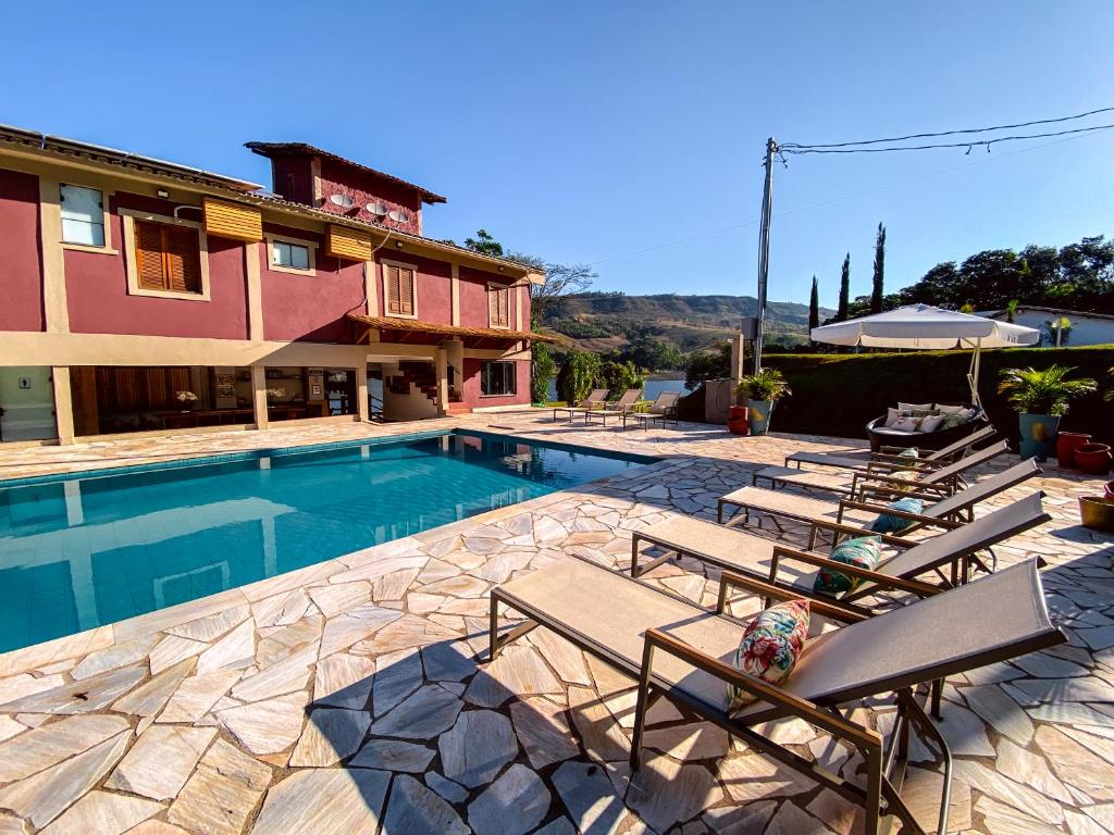 Um pátio de pedra com espreguiçadeiras fica próximo a uma piscina retangular ao lado de uma casa vermelha de dois andares sob um céu azul claro, do Bica D' Água Boutique Hotel. Representa hotéis em Capitólio.