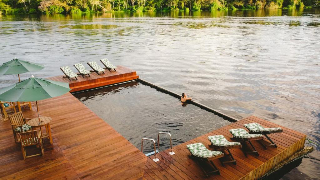 Deck de madeira com espreguiçadeiras e guarda-sóis à beira de um rio, com uma área de natação retangular com uma pessoa na água, do Dolphin Lodge. Representa hotéis em Manaus.