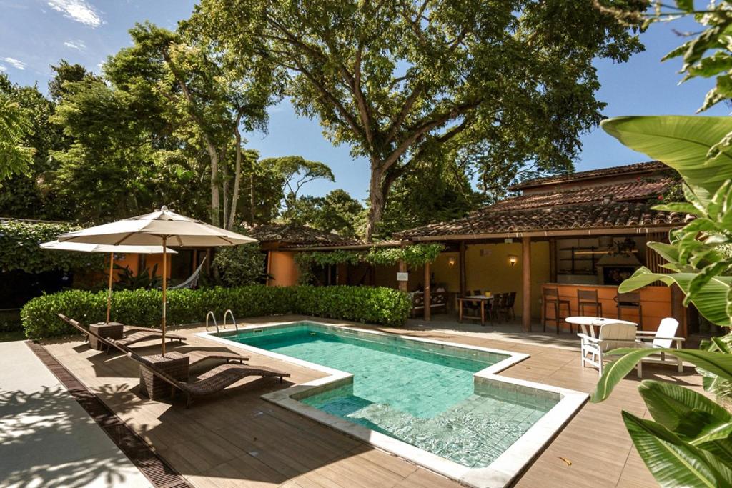 Uma pequena piscina externa com espreguiçadeiras, guarda-sóis e mesas no pátio perto de uma casa cercada por árvores e vegetação, no Estalagem D'Ajuda. Representa hotéis em Arraial d’Ajuda.