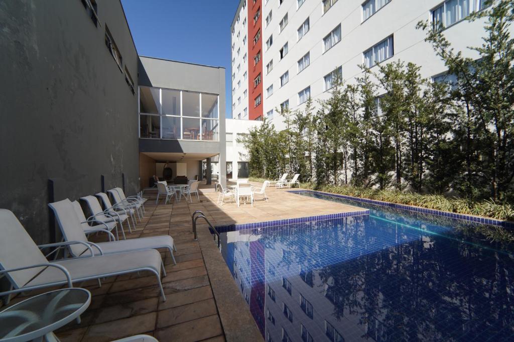 Piscina externa do Hotel Abba Uno ao lado de um moderno prédio de apartamentos, com espreguiçadeiras e mesas dispostas ao longo de um pátio de pedra. Representa hotéis em Contagem.