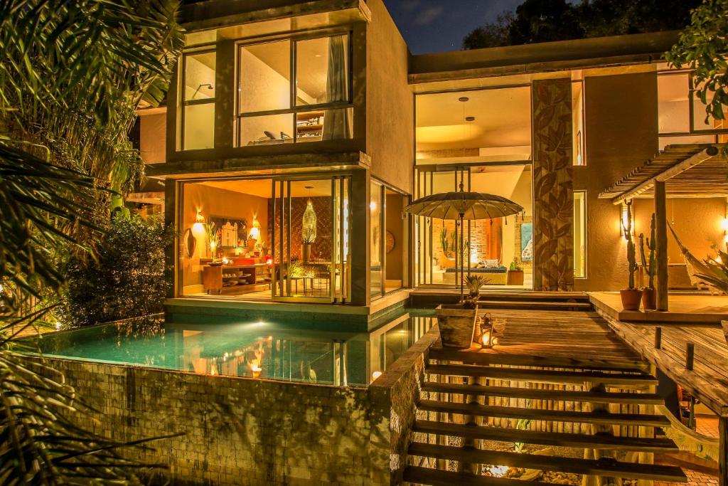 Casa moderna à noite com janelas iluminadas, uma pequena piscina, deck de madeira e escada externa cercada por plantas, do Mercatto Casa Hotel Boutique. Representa hotéis em Arraial d’Ajuda.