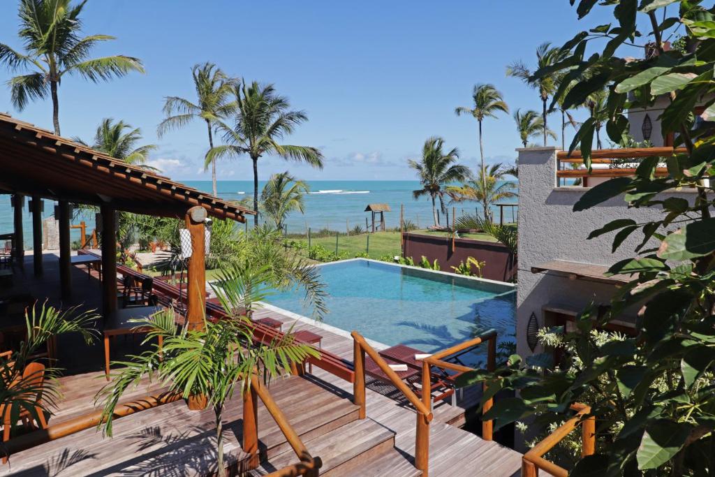 Um deck de madeira com piscina tem vista para o oceano, cercado por palmeiras e edifícios tropicais sob um céu azul claro, do Santa Aldeia Hotel.
