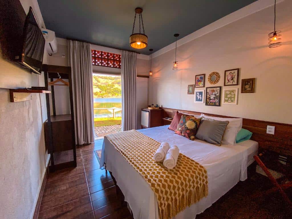 Uma cama bem arrumada com toalhas enroladas em um quarto aconchegante e decorado com arte na parede e vista para um lago do lado de fora, do Bica D' Água Boutique Hotel.