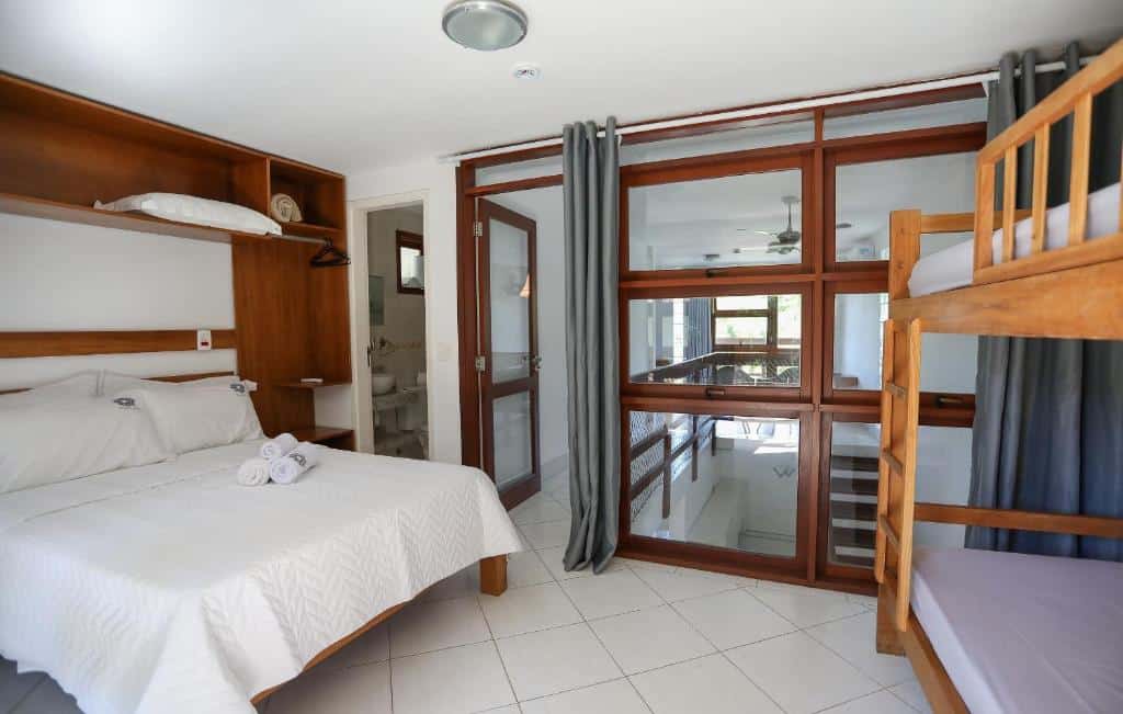 Quarto da Alapage Toque Toque, airbnb em oque-Toque Pequeno, com uma cama de casal, beliche de madeira, piso de azulejo branco, prateleiras e portas de vidro que dão acesso a outro espaço.