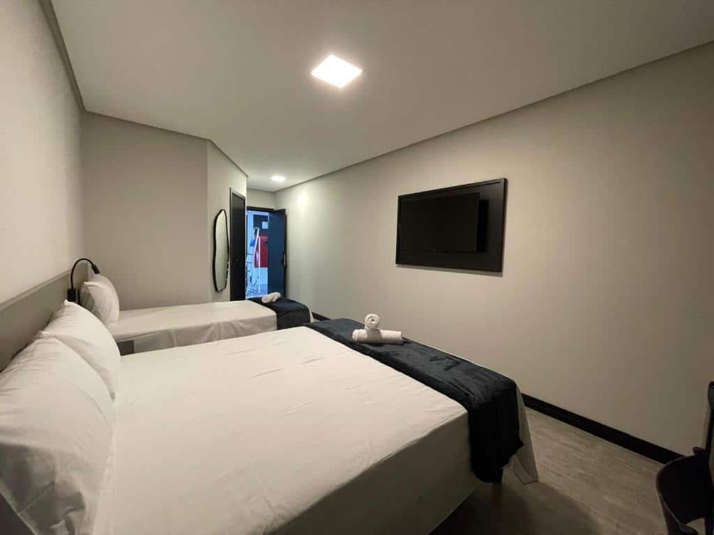 Um quarto do Escarpas Styles Hotel com duas camas, uma TV na parede, paredes brancas e toalhas colocadas em uma cama.