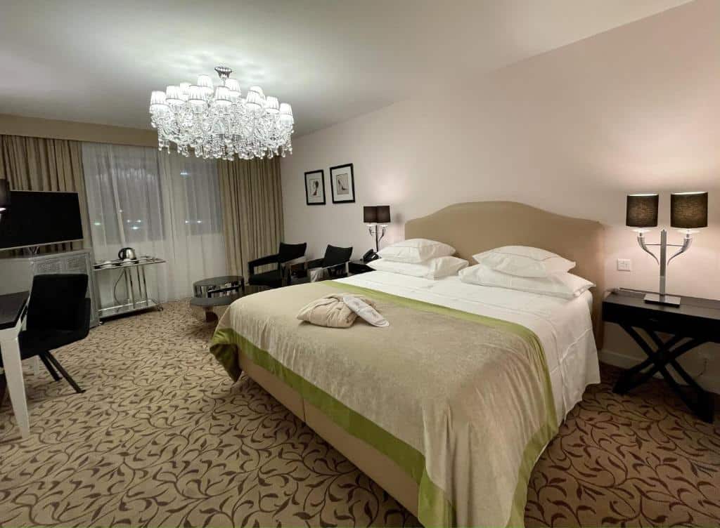 Um quarto do Hotel Adriatica com uma cama de casal, lustre, escrivaninha, TV, duas cadeiras e carpete estampado.