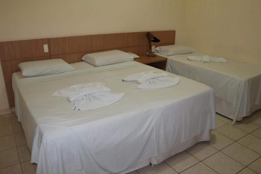 Um quarto do Hotel Mirante Da Ilha com uma cama de casal e uma cama de solteiro, ambas com lençóis brancos e toalhas dobradas em cima.