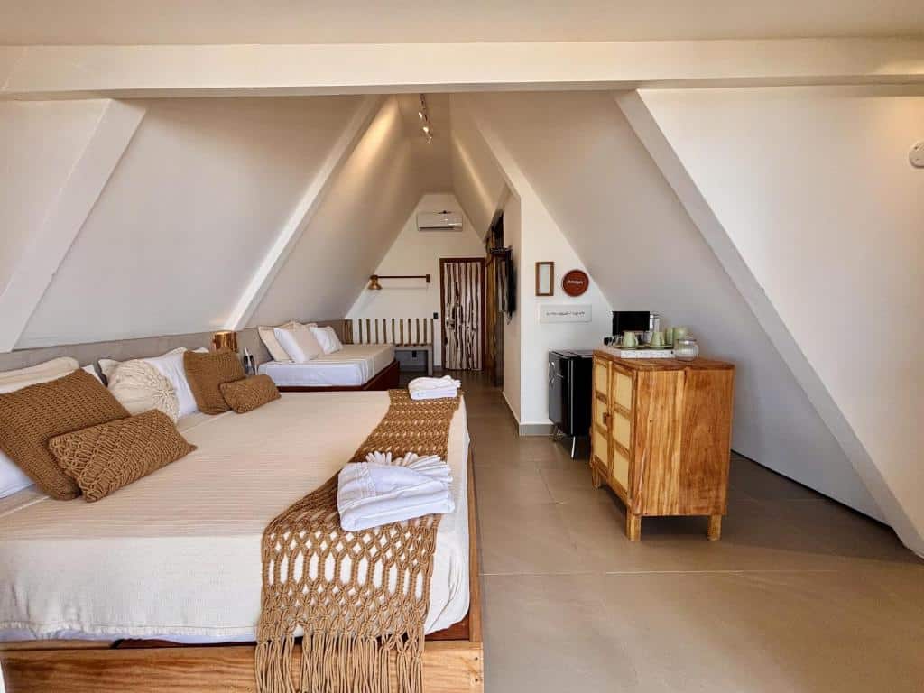 Um quarto moderno do Hotel Pousada Pitinga no sótão com duas camas, decoração bege, cômoda de madeira, frigobar e toalhas dobradas sobre as camas.
