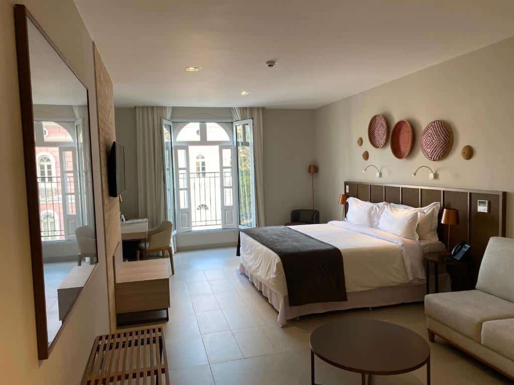 Um quarto do Juma Ópera Boutique Hotel & Spa com uma cama king-size, escrivaninha, TV, poltronas, decoração de parede, janela grande e decoração neutra.