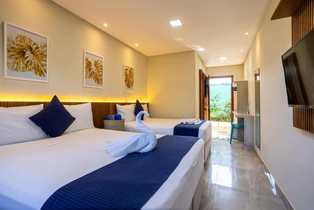 Quarto do Santorini Beach Hotel com duas camas, roupa de cama azul, um cisne de toalha, arte na parede, TV e porta aberta para o exterior.