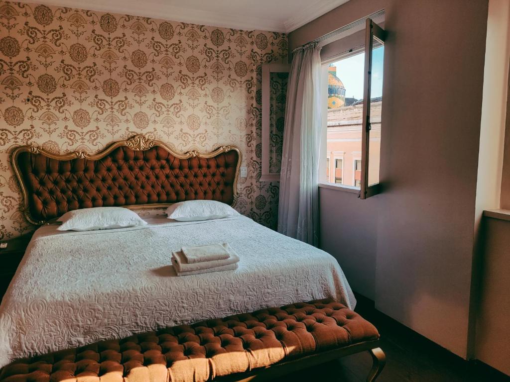 Uma cama bem arrumada com dois travesseiros e toalhas dobradas, ao lado de uma janela aberta que mostrava uma cúpula distante do lado de fora, em Seringal Hotel.