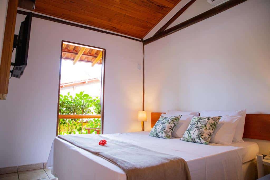Uma cama bem arrumada com lençóis e travesseiros brancos em um quarto simples com uma janela, teto de madeira e uma pequena lâmpada, do Tororao Hotel Pousada.