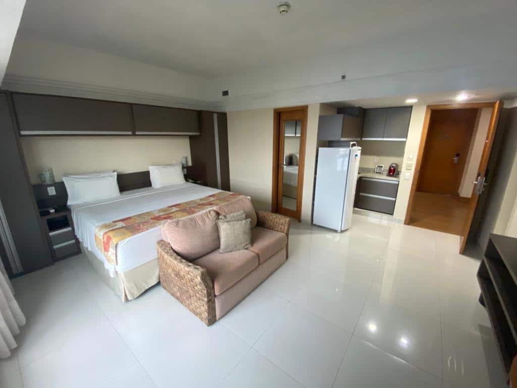 Um quarto do Tropical Executive Hotel com uma cama king-size, um pequeno sofá, uma área de cozinha e um piso de azulejos brancos.